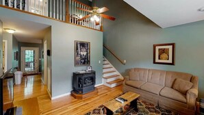 Ein geräumiges Wohnzimmer mit Holzboden, einem beige farbenen Sofa, einem gemusterten Teppich, einem Kamin und einer Treppe mit Geländer.