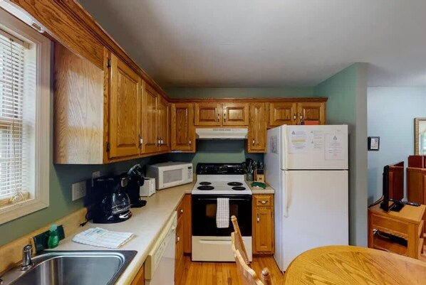 Cocina pequeña con gabinetes de madera, estufa, microondas y refrigerador.