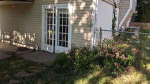 Een huis met een veranda, een schuifdeur en een kleine tuin met roze bloemen.