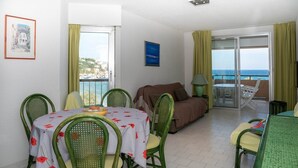 Une pièce comprenant une table à manger, des chaises, un canapé et un balcon avec vue sur la mer.