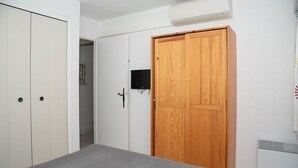 Une chambre à coucher comprenant un lit, une armoire en bois, une armoire blanche et un téléviseur fixé au mur.