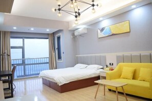 A hotel room with a bed, a yellow sofa, a small table, a balcony with a railing, and a window.