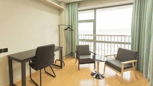 A room with a desk, two chairs, a hanging light, and a large window with curtains. - Mango Hotel (Bengbu)
