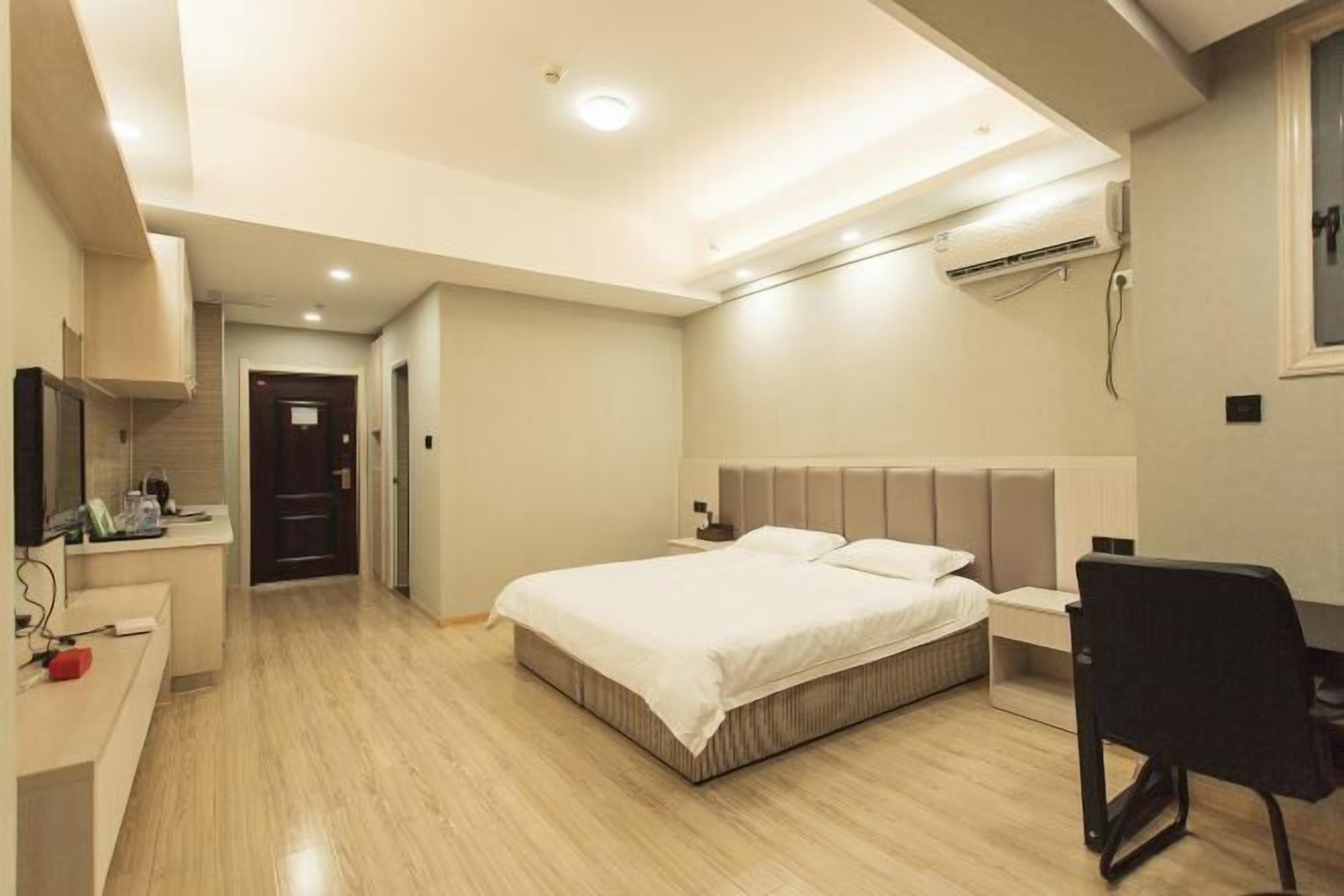 A bedroom with a bed, bedside table, desk, chair, and an air conditioning unit.