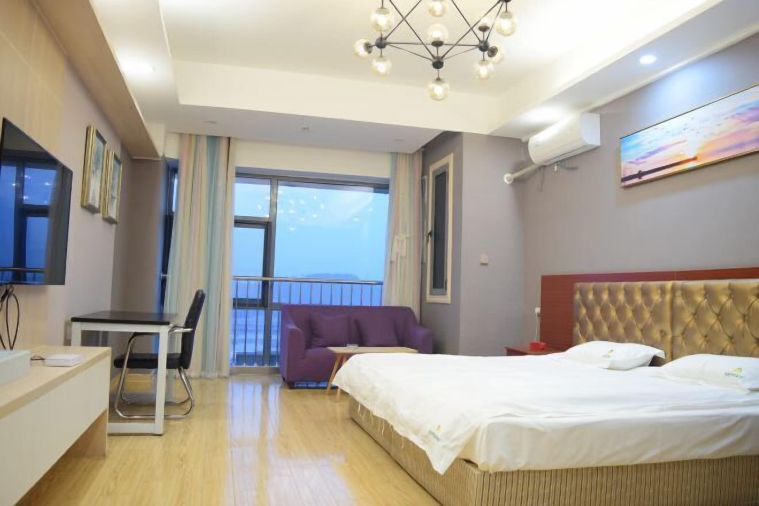 Hotellihuone, jossa on sänky, työpöytä, tuoli, violetti sohva ja suuri ikkuna.