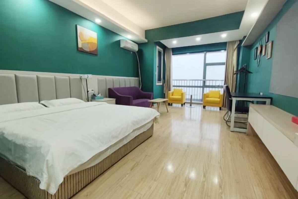 Habitación de hotel con una cama grande, un escritorio, dos sillas y un balcón con vistas.