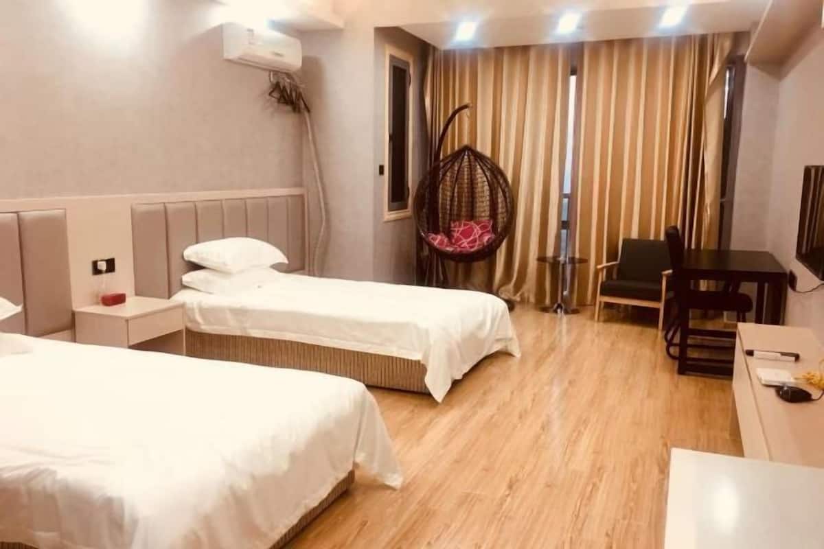 Habitación de hotel con dos camas, un escritorio, una silla, un sillón colgante y una ventana con cortinas.