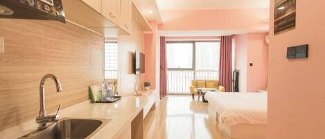 Una habitación de hotel moderna con kitchenette, un ventanal con cortinas, una cama y un televisor.