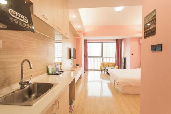 A modern hotel room with a kitchenette, a large window with curtains, a bed, and a TV.