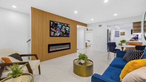 A modern living room with a TV mounted on a wooden wall, a fireplace, and a dining area in the background. - 10 BEDS, 4 BATHS, Sleep 16 in the most Prime Location in Miami!  (Miami)