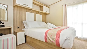 Ein Schlafzimmer mit Bett, Nachttischen, einem Kleiderschrank, einem Spiegel und einem Fenster mit Vorhängen.