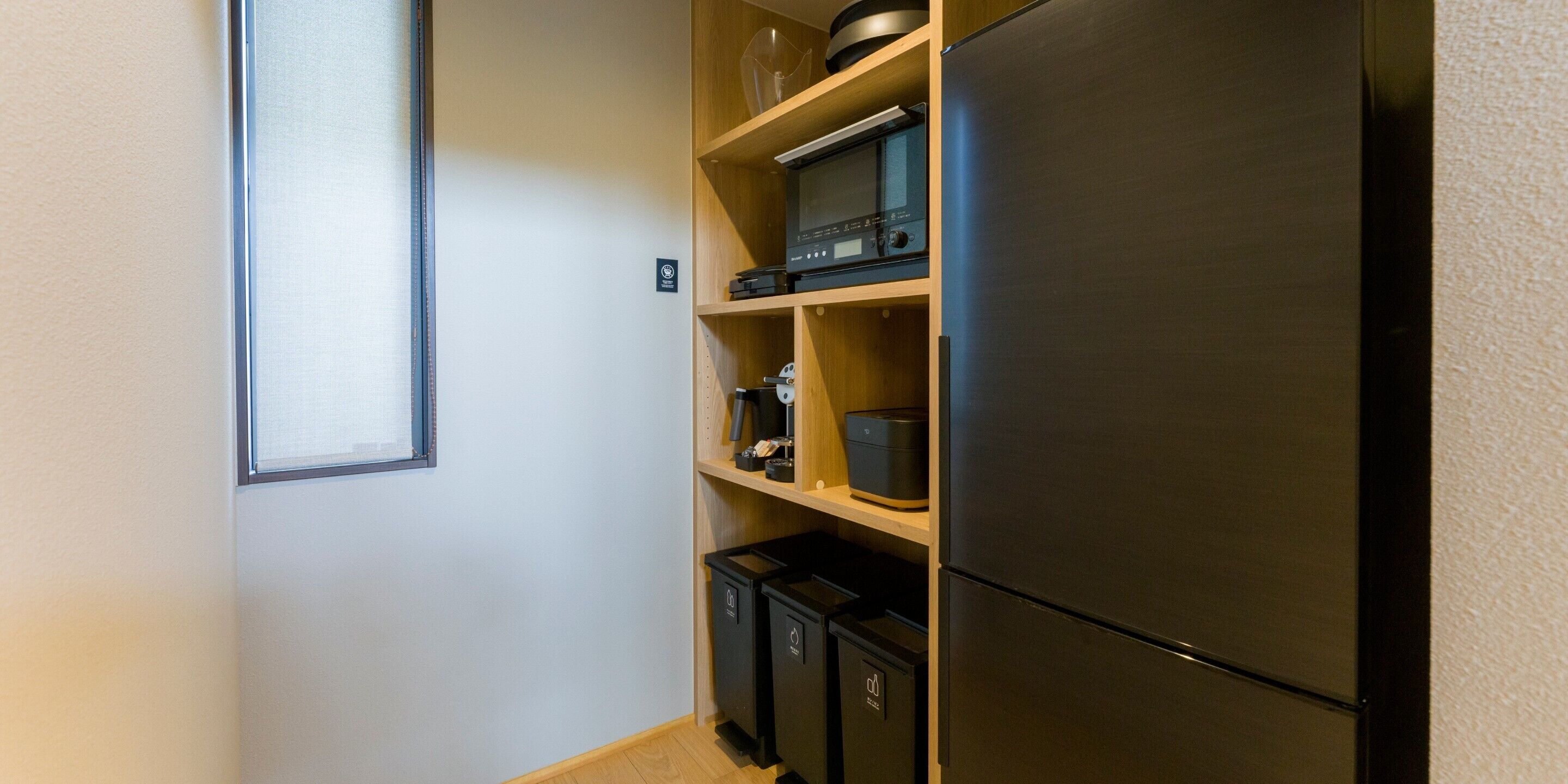 A compact kitchen with a built-in refrigerator, wooden shelves, and a microwave.