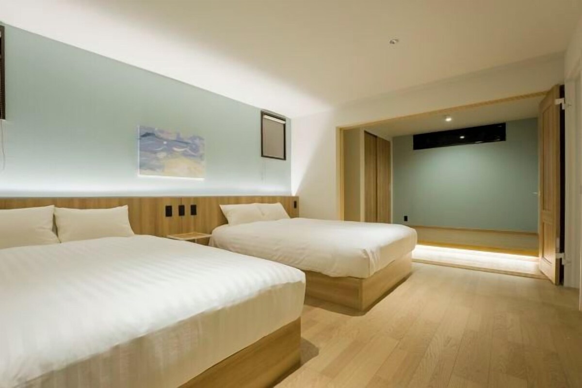 A hotel room with two beds, a wooden headboard, a painting on the wall, and a door leading to another room.