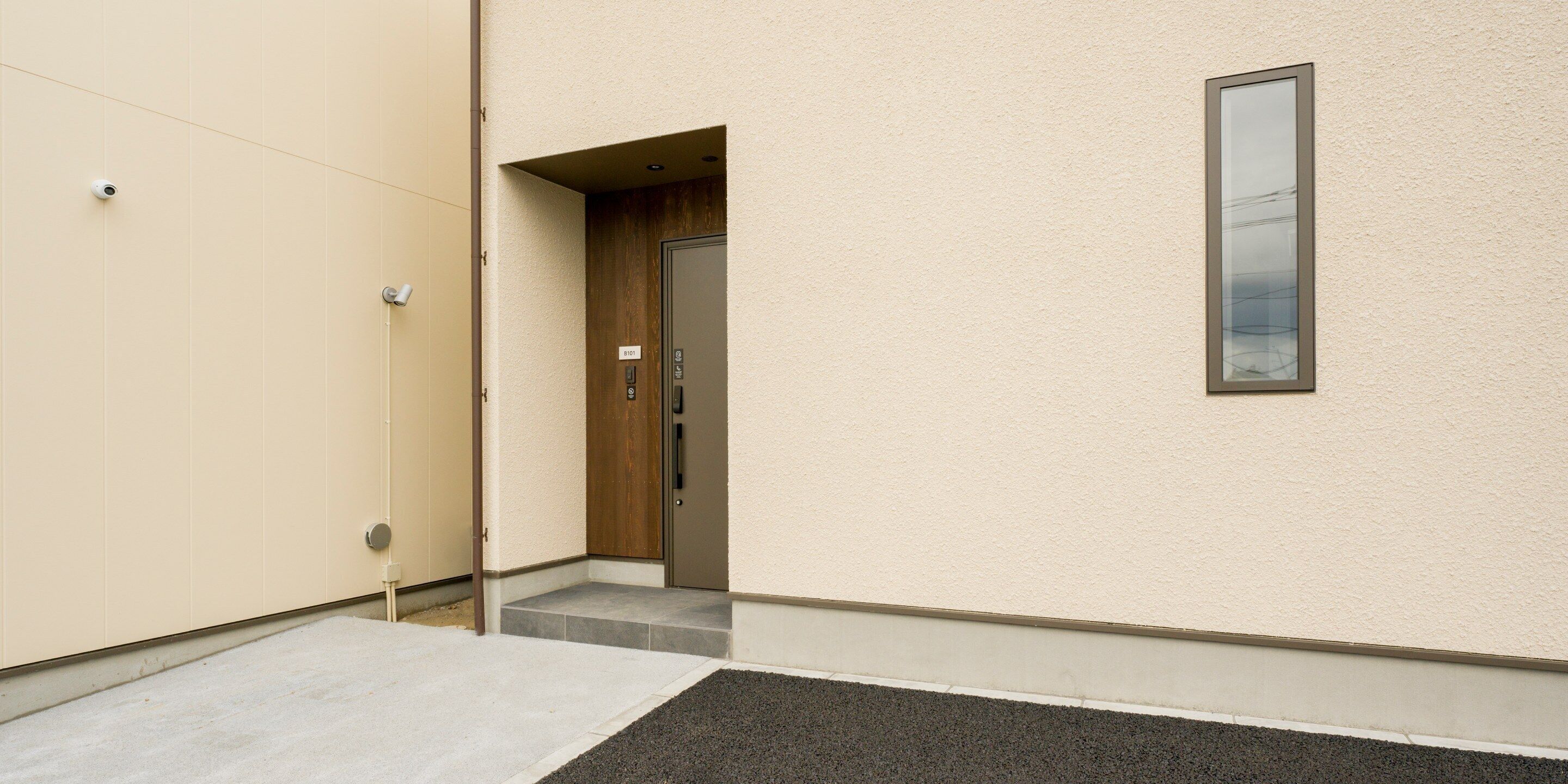 Une entrée d’immeuble avec une porte en bois, une petite fenêtre et une caméra de surveillance.