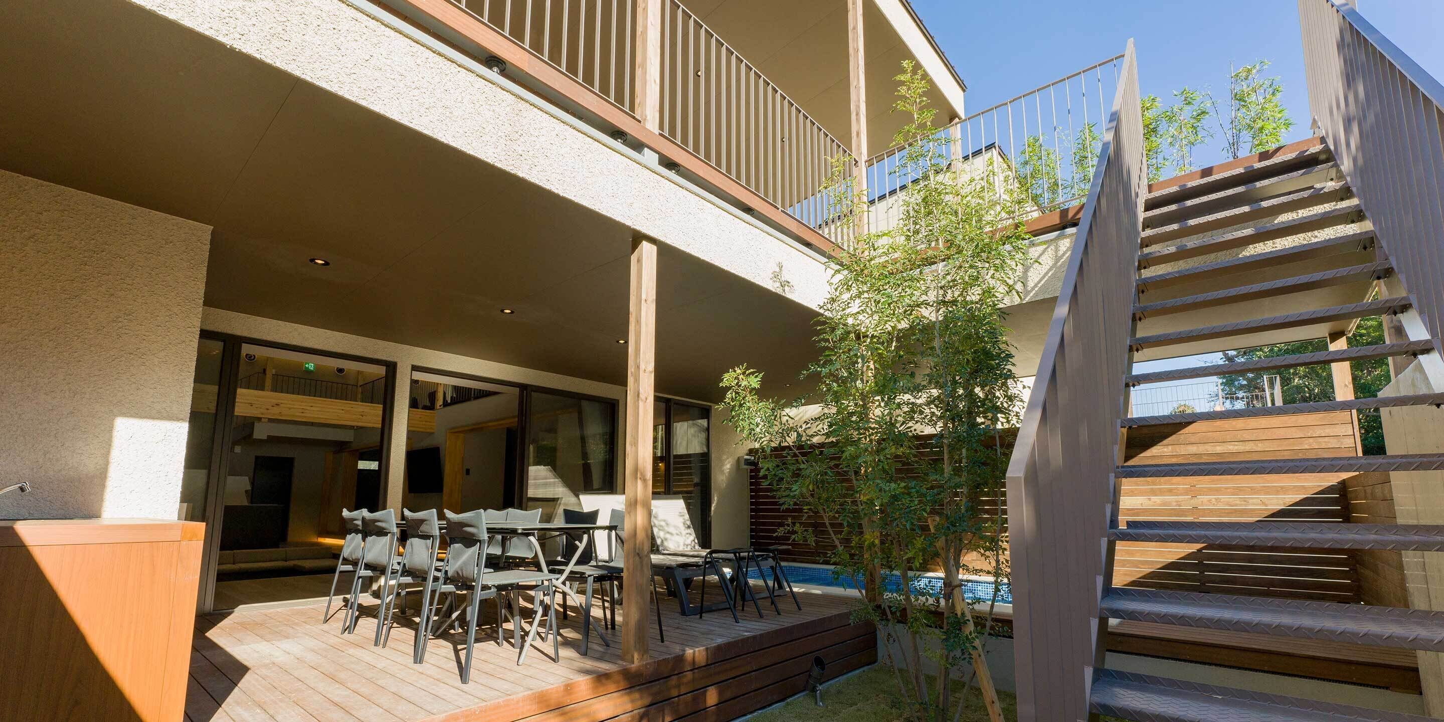 A modern outdoor patio with a pool, wooden deck, and a staircase leading to an upper level.