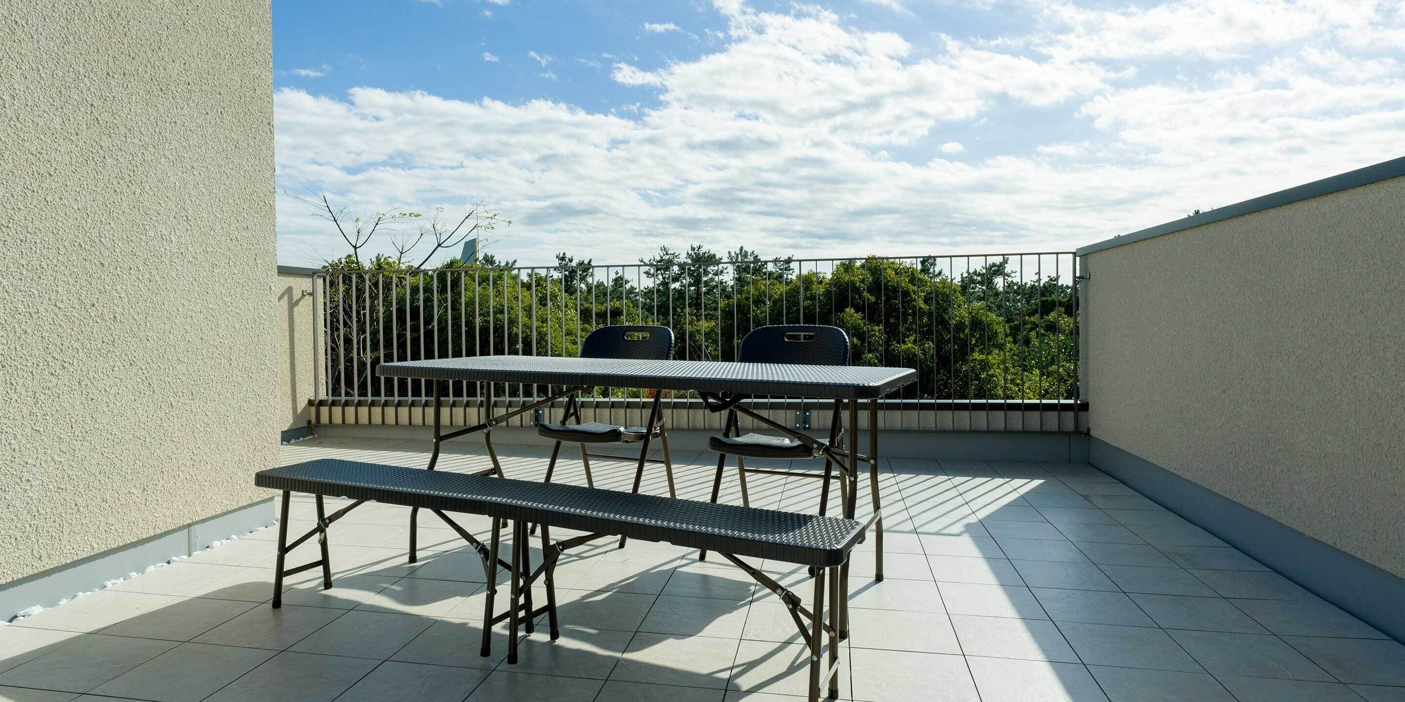 A balcony with a metal table and bench, a railing, and a view of trees and sky.