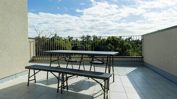 Un balcon avec une table et un banc en métal, une balustrade et une vue sur les arbres et le ciel.
