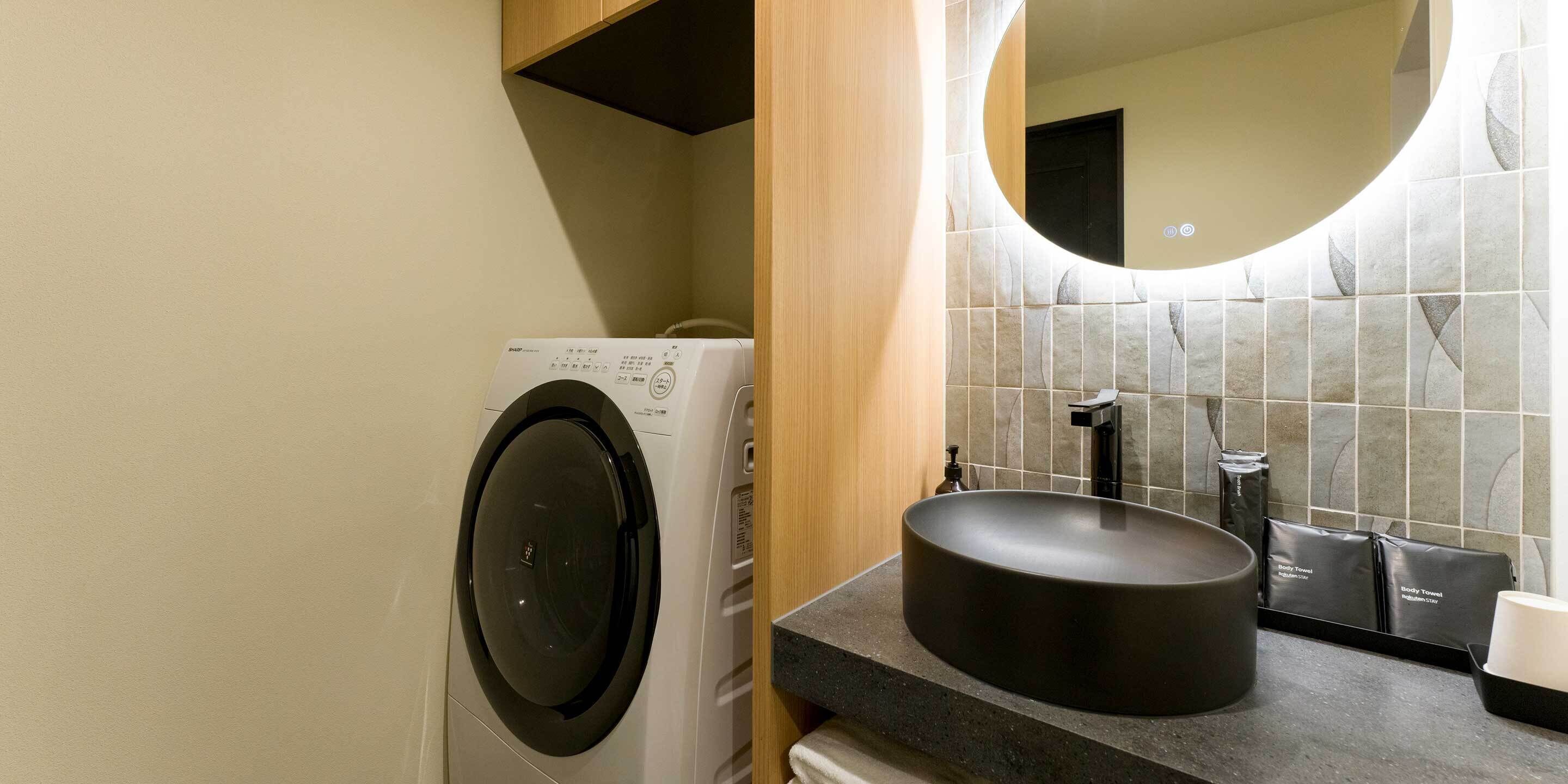 A compact bathroom with a washing machine, a sink, and a mirror.