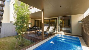 Uma área de piscina moderna ao ar livre, com um deck de madeira, espreguiçadeiras e um pequeno jardim.