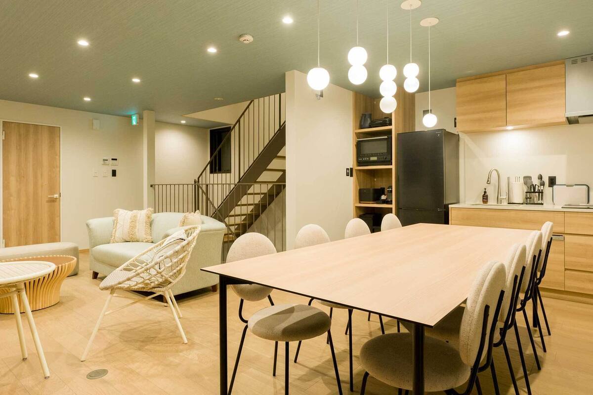 A modern kitchen with a dining area, wooden cabinets, and a staircase leading to another level.