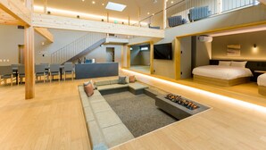 Interior moderno de hotel com área de estar central, escada e quarto com cama e mesa de cabeceira.