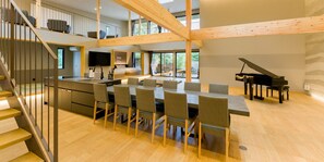 A spacious living area with a dining table, chairs, a piano, and a kitchen area. - Rakuten STAY VILLA Kamogawa (Kamogawa)