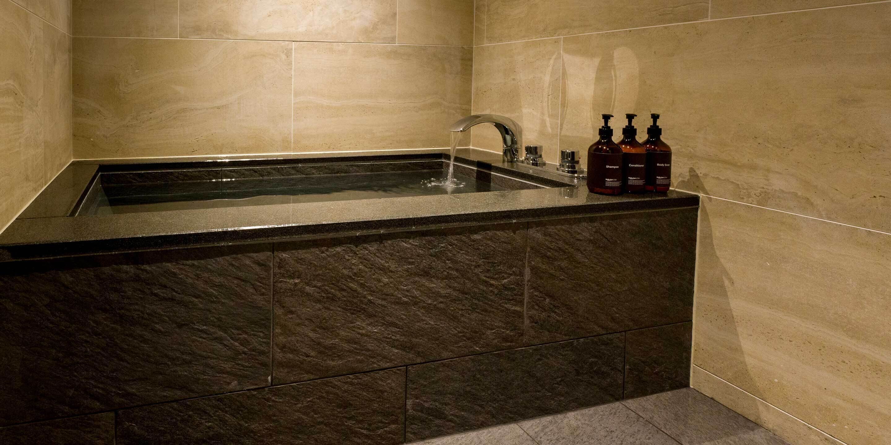 A bathroom with a marble sink, a modern faucet, and three bottles of shampoo and conditioner on the counter.