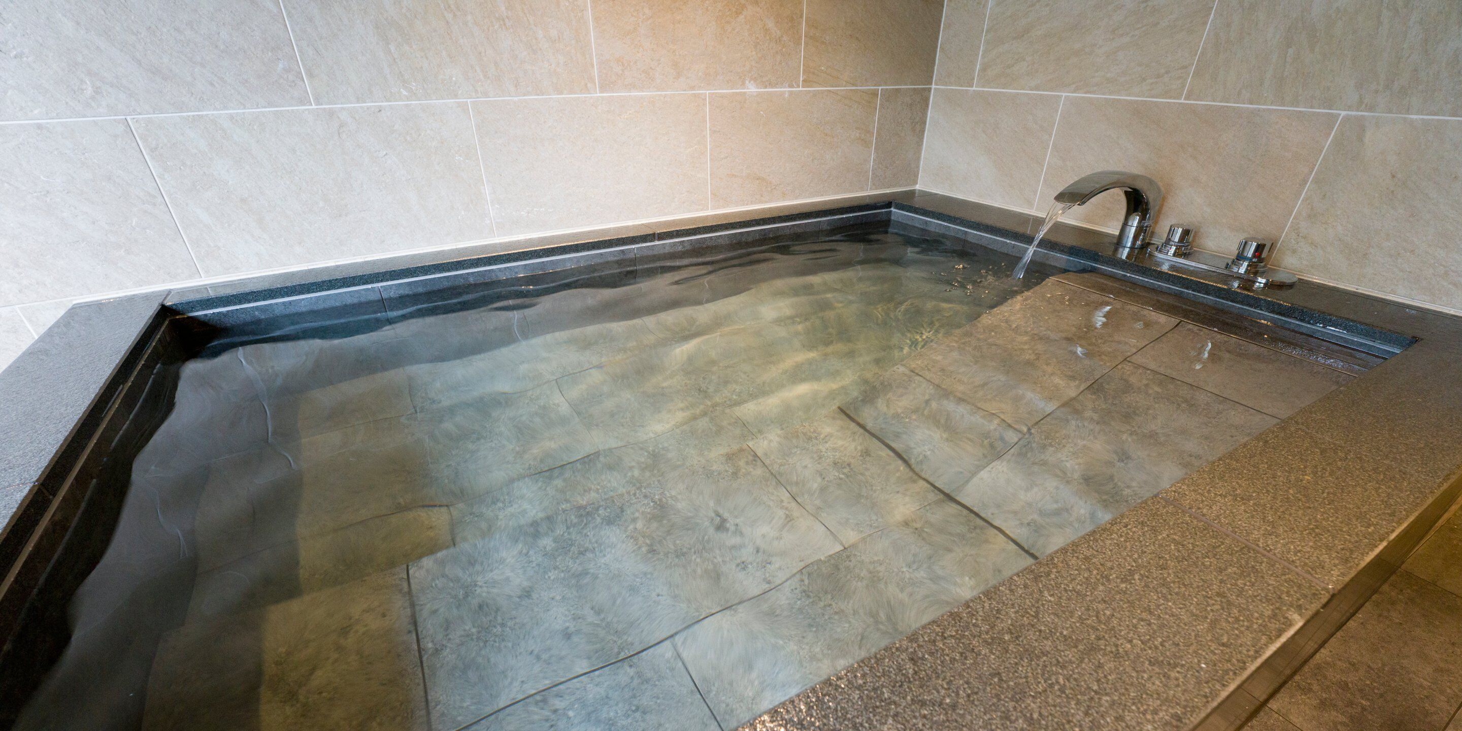 Un bain à remous rectangulaire doté d’un bord noir, d’un robinet et d’un jet d’eau.