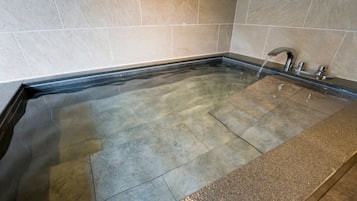 Un bain à remous rectangulaire doté d’un bord noir, d’un robinet et d’un jet d’eau.