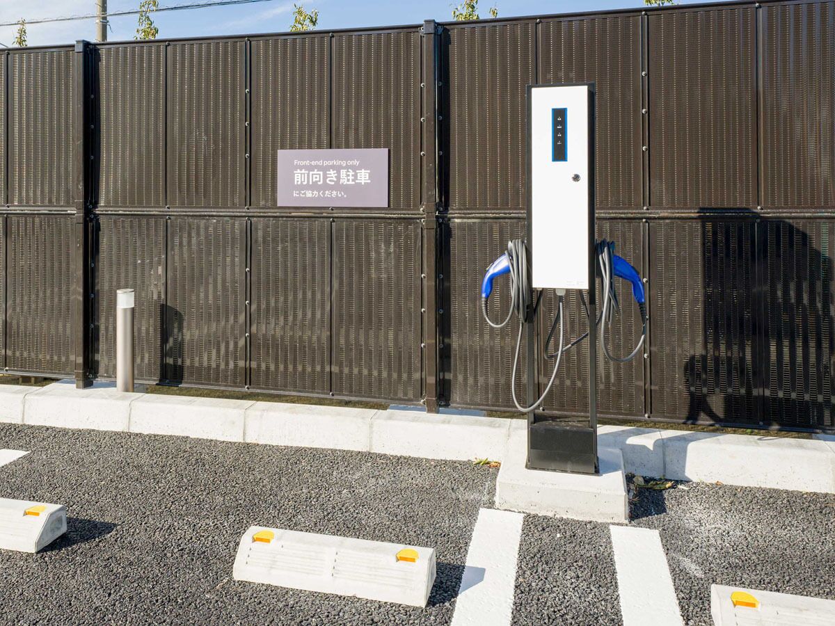 Un área de estacionamiento con un cartel que indica acceso solo para vehículos por la parte delantera, una estación de carga y una valla metálica.