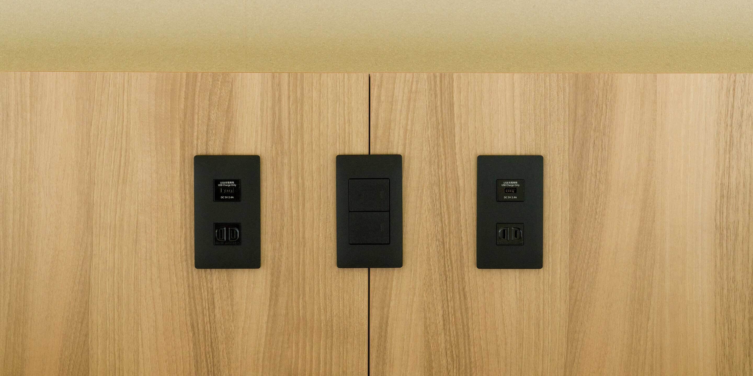 Three black electrical outlets on a wooden wall.