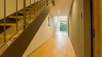 Ein modernes Interieur mit einer Holztreppe, einem zur Tür führenden Flur und Blick ins Grüne.
