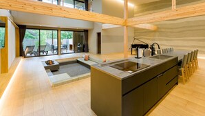 Uma cozinha moderna com uma ilha central, uma área de jantar com cadeiras e um piano ao fundo.