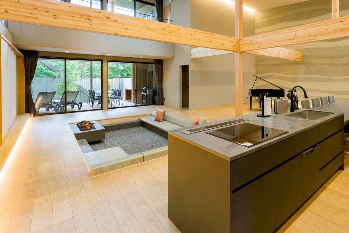 A modern kitchen with a central island, a dining area with chairs, and a piano in the background.