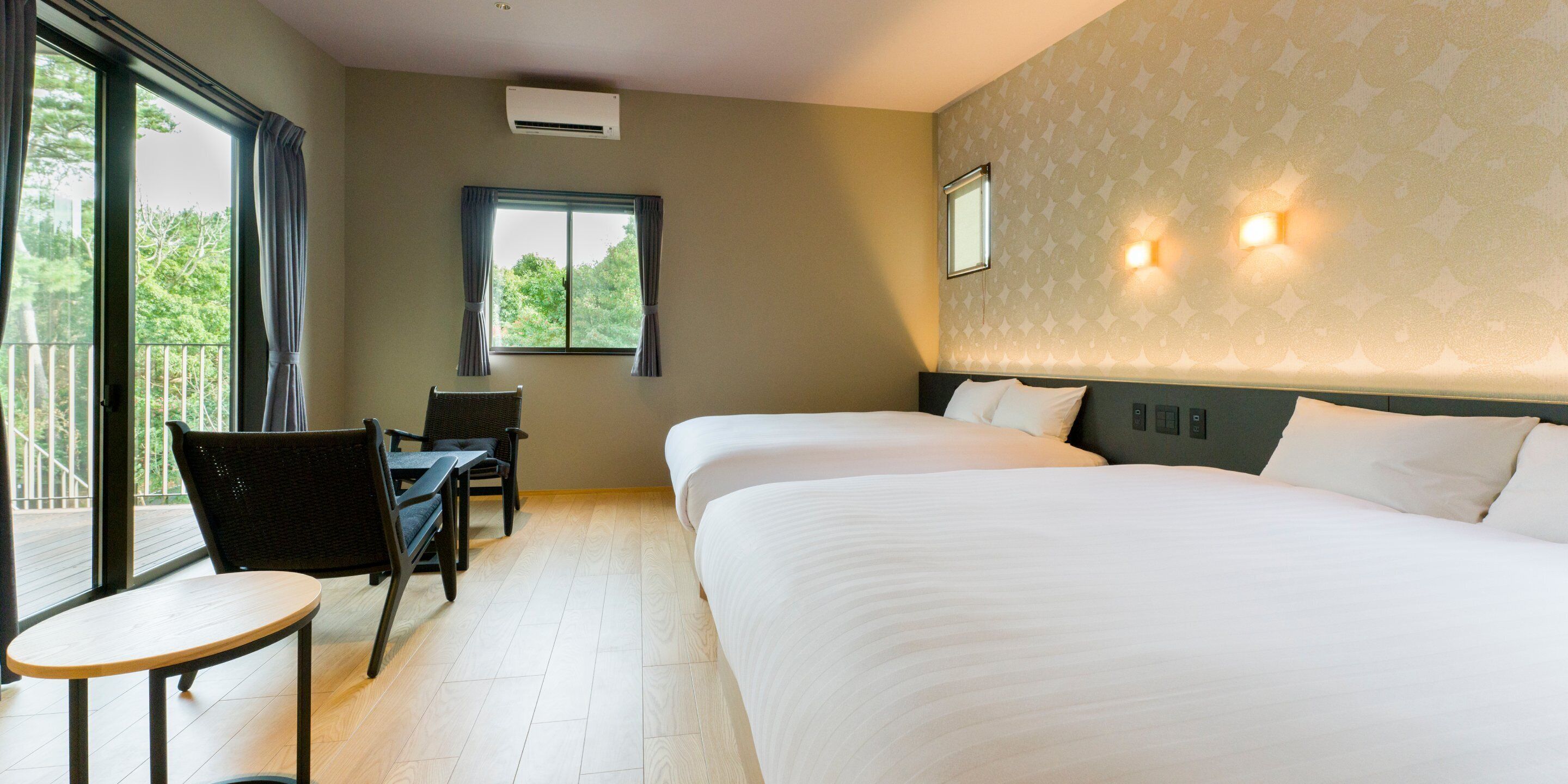Une chambre d’hôtel avec deux lits, une petite table, une chaise, une fenêtre avec des rideaux et un climatiseur fixé au mur.