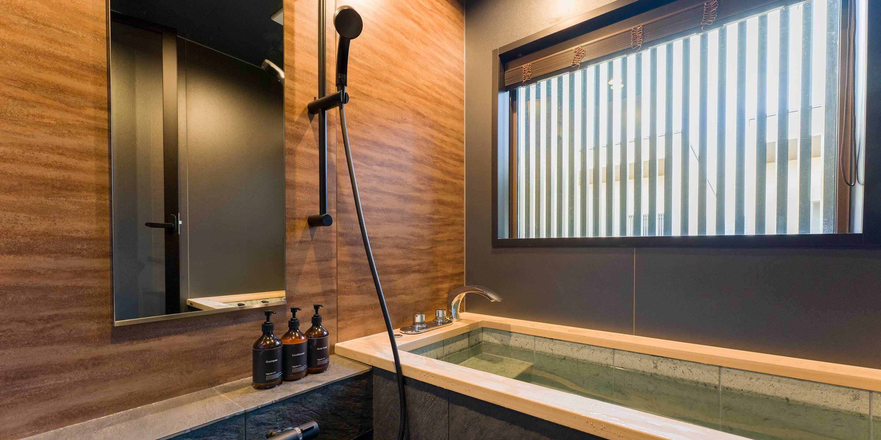 A modern bathroom with a glass-enclosed bathtub, a large mirror, and a window with vertical blinds.