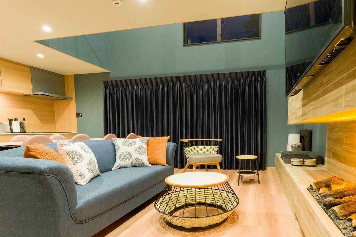 A modern living room with a blue sofa, a round wicker coffee table, and a fireplace.
