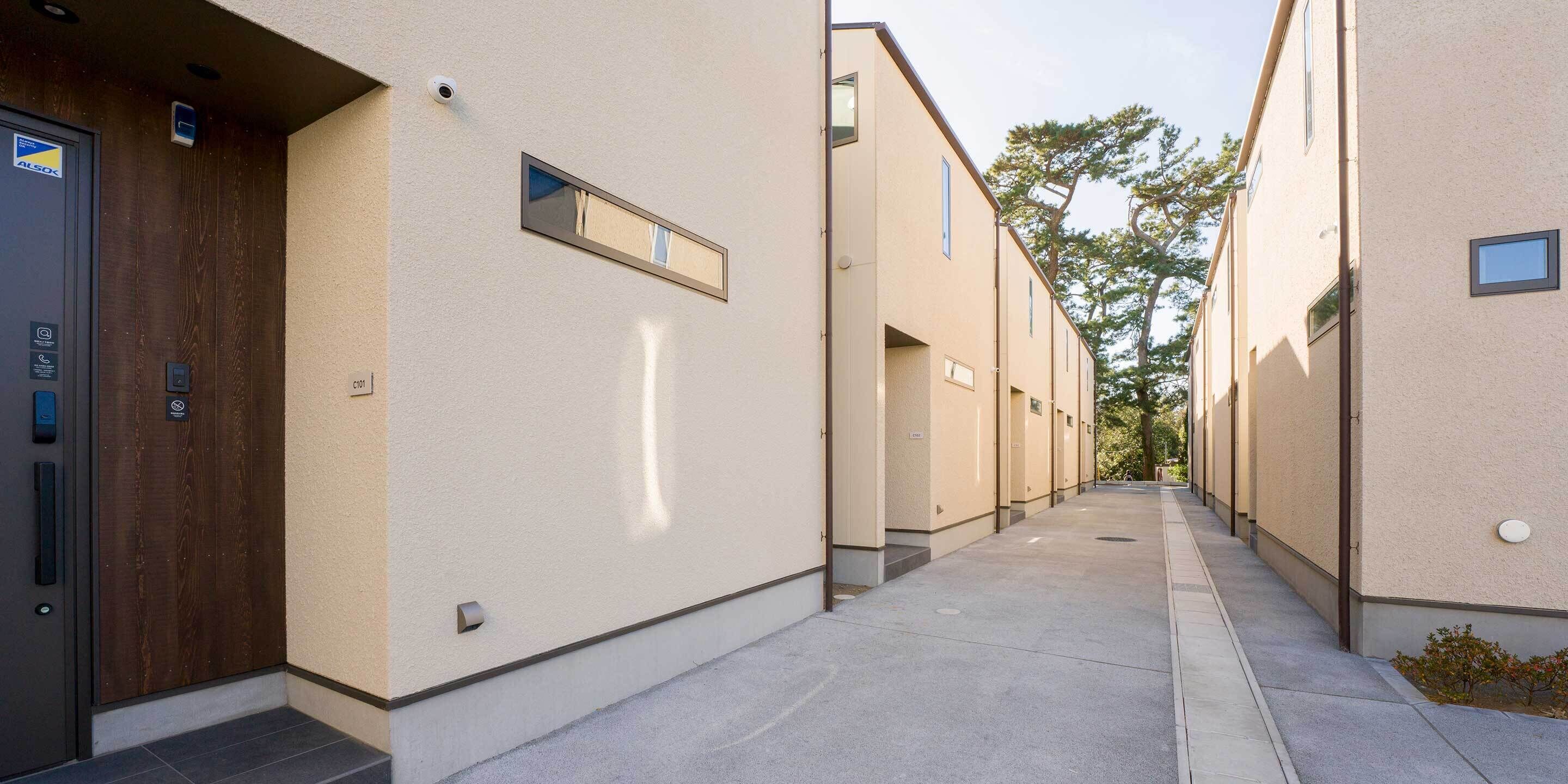 A corridor with a wooden door on the left, a security camera above, and a small window on the right wall.