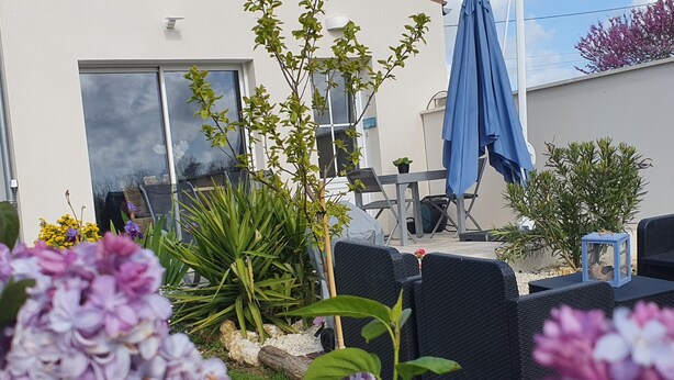 Un patio con mobiliario exterior, una sombrilla azul y varias plantas.