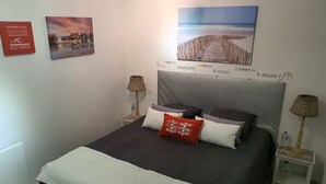 Un dormitorio ordenado con cama, almohadas, mesita de noche, lámpara y decoración en la pared.