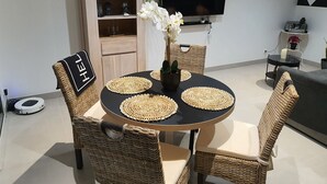 Un comedor con una mesa redonda, sillas tejidas y un florero con flores.