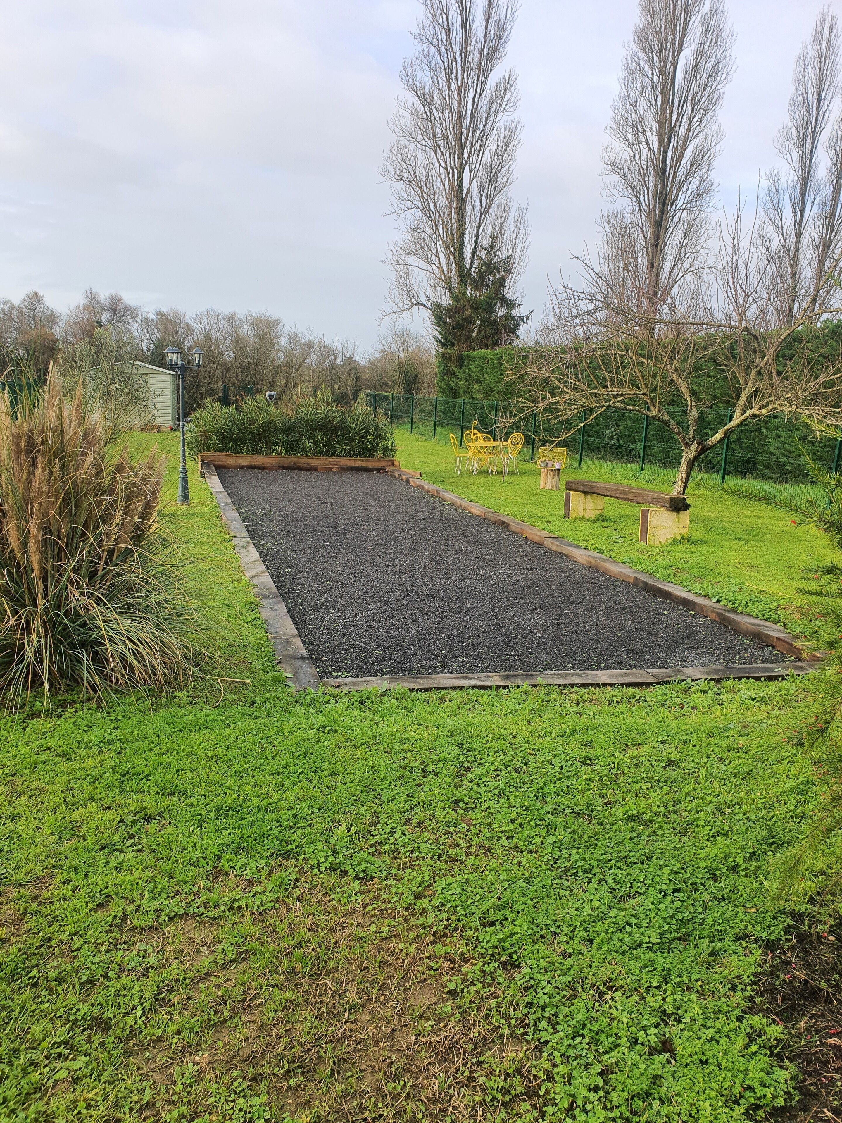 A rectangular outdoor area with a gravel surface, surrounded by green grass and various plants.