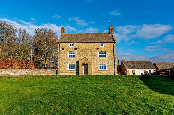 Une maison en pierre avec une entrée centrale, de nombreuses fenêtres et une cheminée.