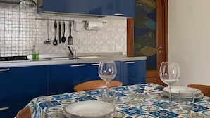 Een keuken met blauwe kastjes, een betegelde spatwand en een eethoek met een tafelkleed met dessin.