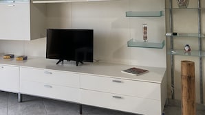Een moderne woonkamer met een flatscreen televisie, witte kasten, glazen planken en een houten accent.