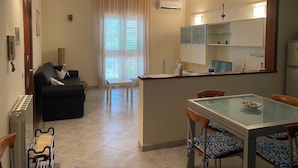 Een knus woongedeelte met een kitchenette, een eethoek met een glazen tafel en een zithoek met een bank en fauteuils.