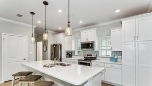 A modern kitchen with white cabinetry, a central island with stools, stainless steel appliances, and pendant lighting. - Best Views of the Gulf and Lost Key Beach Club From Your Private Townhome Balcony | 4 Bikes | Pools (Pensacola)