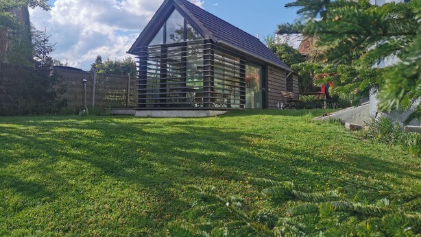 A modern house with a sloped roof and large windows, surrounded by a well-maintained lawn and trees. - Bauernhäusle - the house with a beautiful garden (Friedrichshafen)
