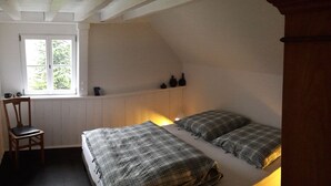 A bedroom with a sloped ceiling, a bed with plaid bedding, a chair, and a window with a view of greenery. - Bauernhäusle - the house with a beautiful garden (Friedrichshafen)