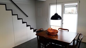 A dining area with a wooden table and chairs, a woven basket, a black pendant light, and a staircase with black steps. - Bauernhäusle - the house with a beautiful garden (Friedrichshafen)